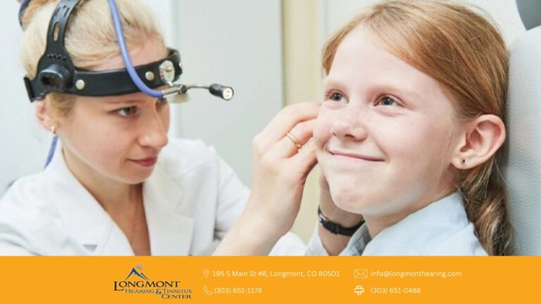 An image of a girl smiling while being checked on her ear with a woman on white coat with a head lamp.